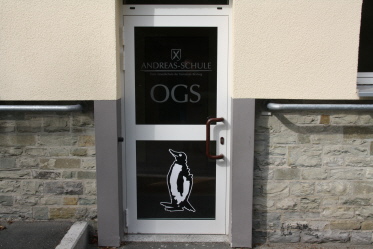 Foto OGS-Eingangstür mit den Hinweisbeschriftungen und dem Pinguin als OGS-Maskottchen