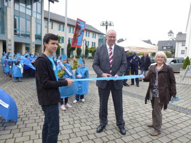 Der Bürgermeister eröffnet durch Durchscneiden eines blauen Bandes die Ausstellung.